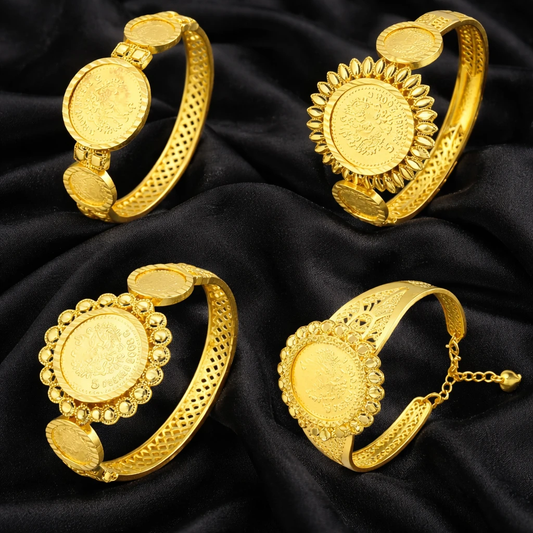 Four gold bracelets with intricate designs on a black fabric background