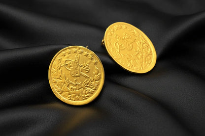 Two gold coins with embossed designs on a dark surface.