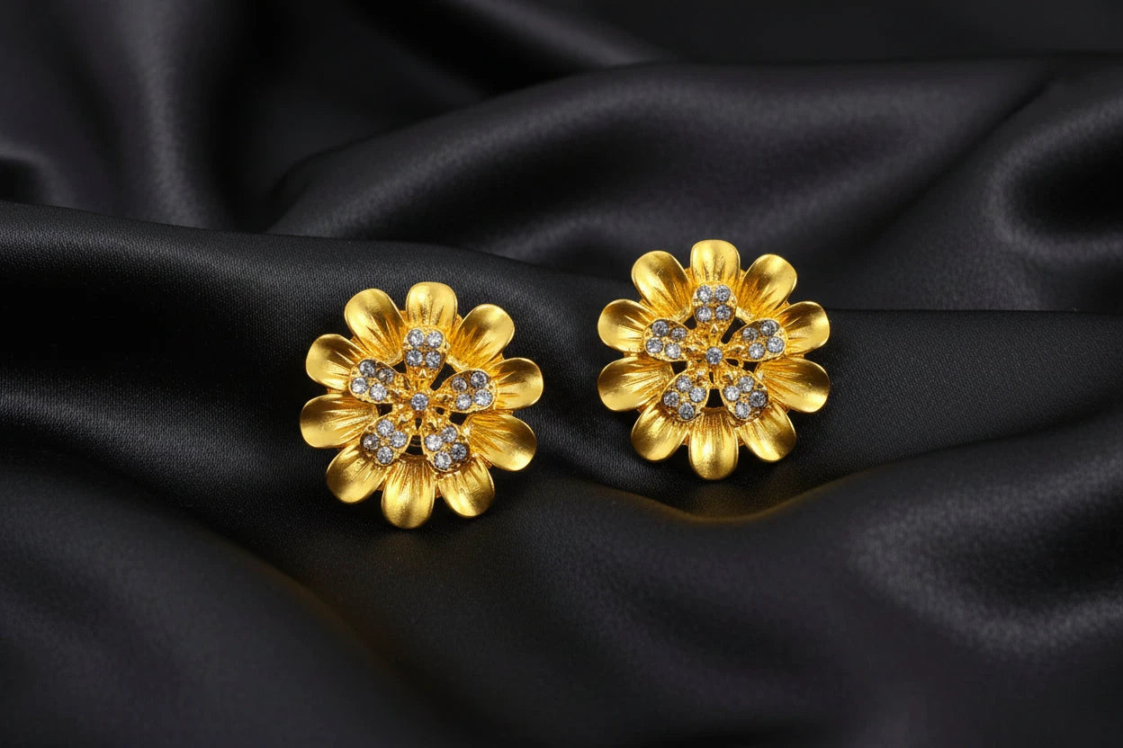 Gold flower-shaped earrings with gemstones with black background.