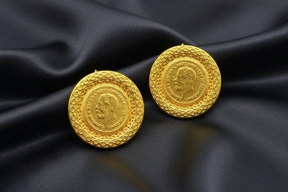 Two gold coins with embossed faces on a dark surface.